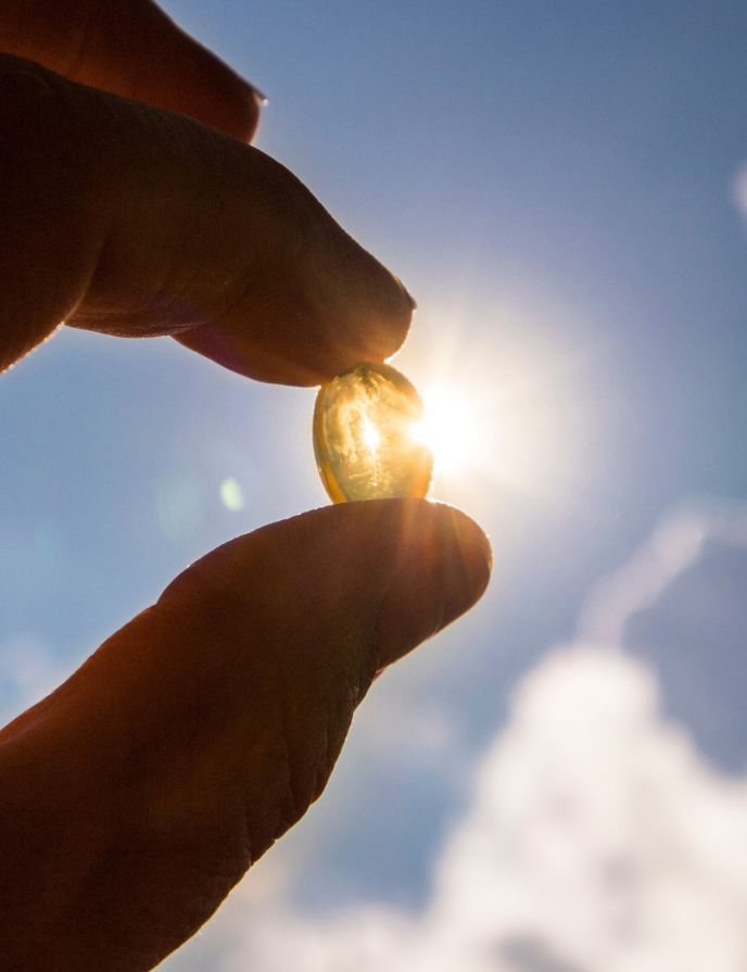 Vitamin-D-Messung Hand hält eine Vitamin-D-Kapsel gegen die strahlende Sonne – Symbol für Vitamin-D-Messung und Beratung in der Balance Apotheke.